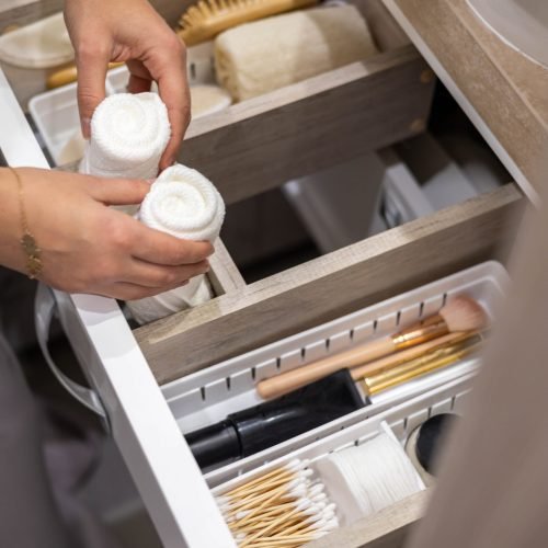 Top view of woman hands neatly organizing bathroom amenities and toiletries in drawer or cupboard in bathroom. Concept of tidying up a bathroom storage by using Marie Kondo's method.